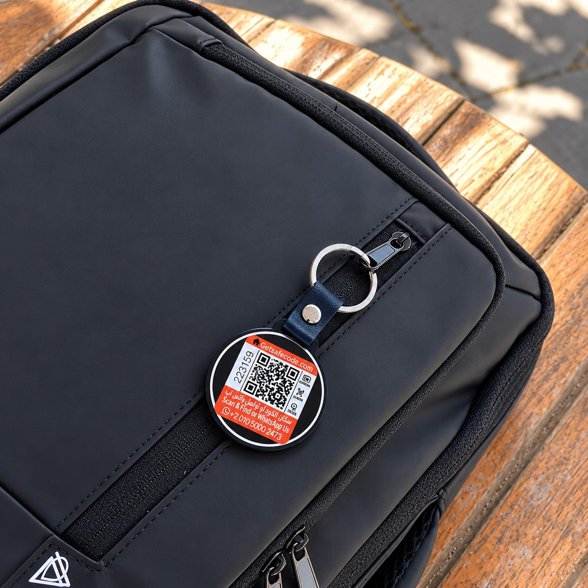 Safe Code QR bag tag clipped to the zipper of a black backpack